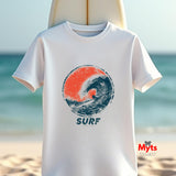 A white short-sleeve t-shirt with a circular surf graphic in orange and navy blue, featuring the word 'SURF' underneath, displayed against a blurred beach background.