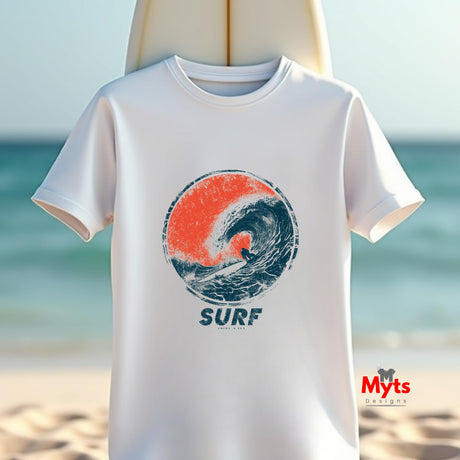 A white short-sleeve t-shirt with a circular surf graphic in orange and navy blue, featuring the word 'SURF' underneath, displayed against a blurred beach background.