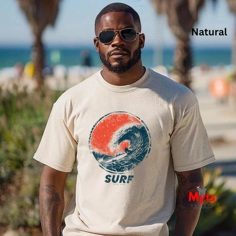 A man wearing a Natural t-shirt with a circular surf graphic and the word 'SURF' printed below it, standing outdoors near a beach with palm trees in the background.
