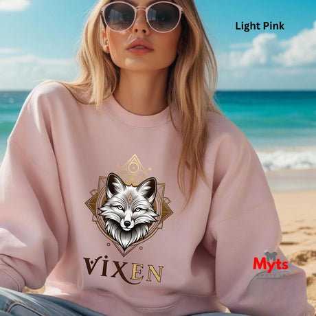 Woman wearing a pink sweatshirt with a fox design and 'Vixen' text on a beach.